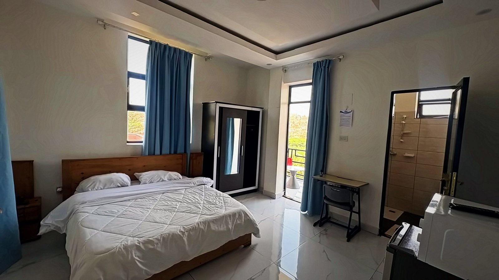 Bedroom with a wooden-headboard bed, blue curtains, a wardrobe and a desk at Holy Apartments, Kigali