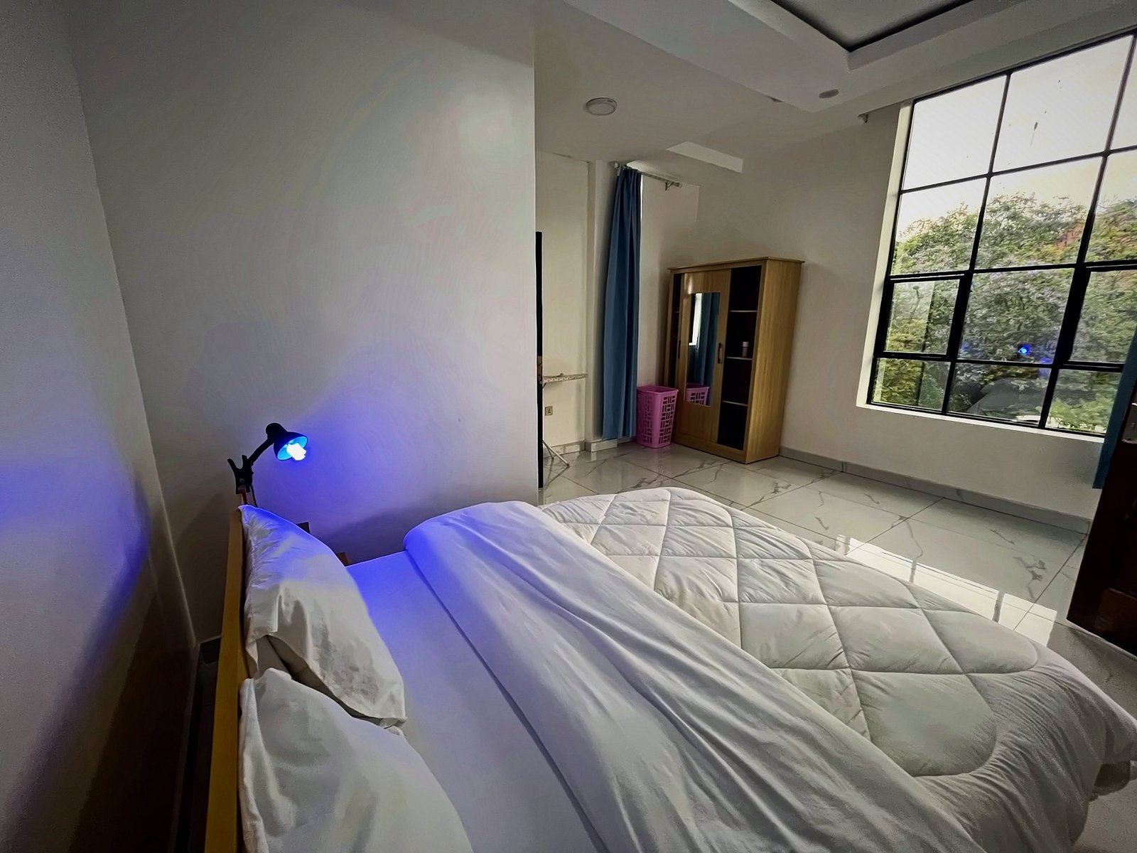 Bedroom with a large bed and a big window overlooking trees at Holy Apartments, Kigali