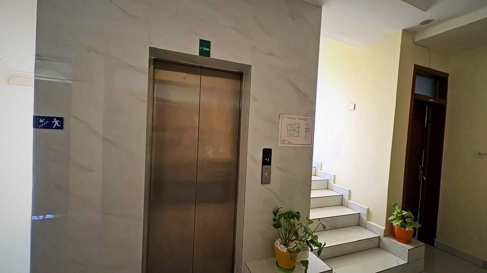 Lift lobby with a stainless-steel lift and a marble staircase at Holy Apartments, Kigali