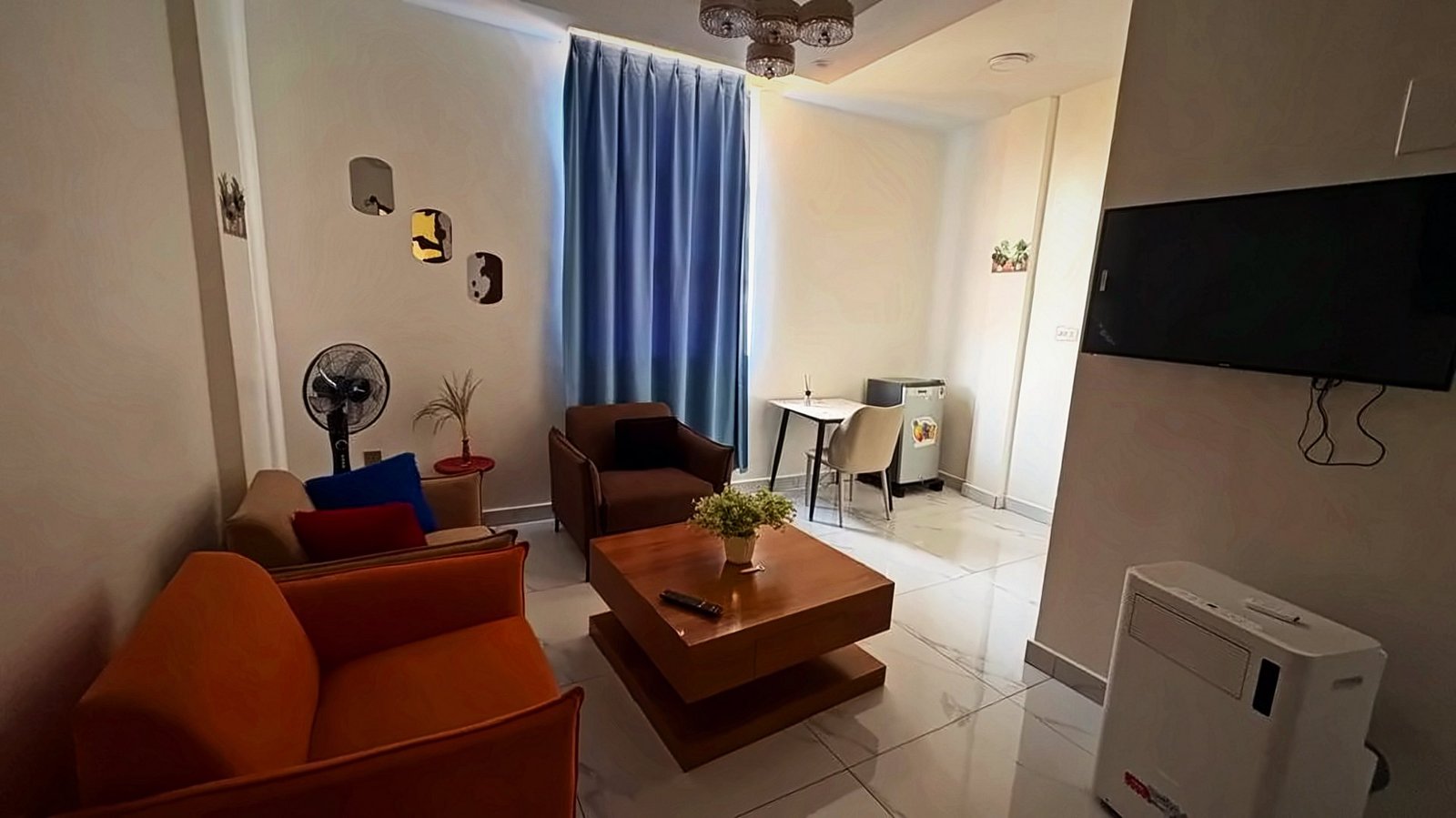 Living room with an orange sofa, armchair, wooden coffee table and wall-mounted TV at Holy Apartments, Kigali