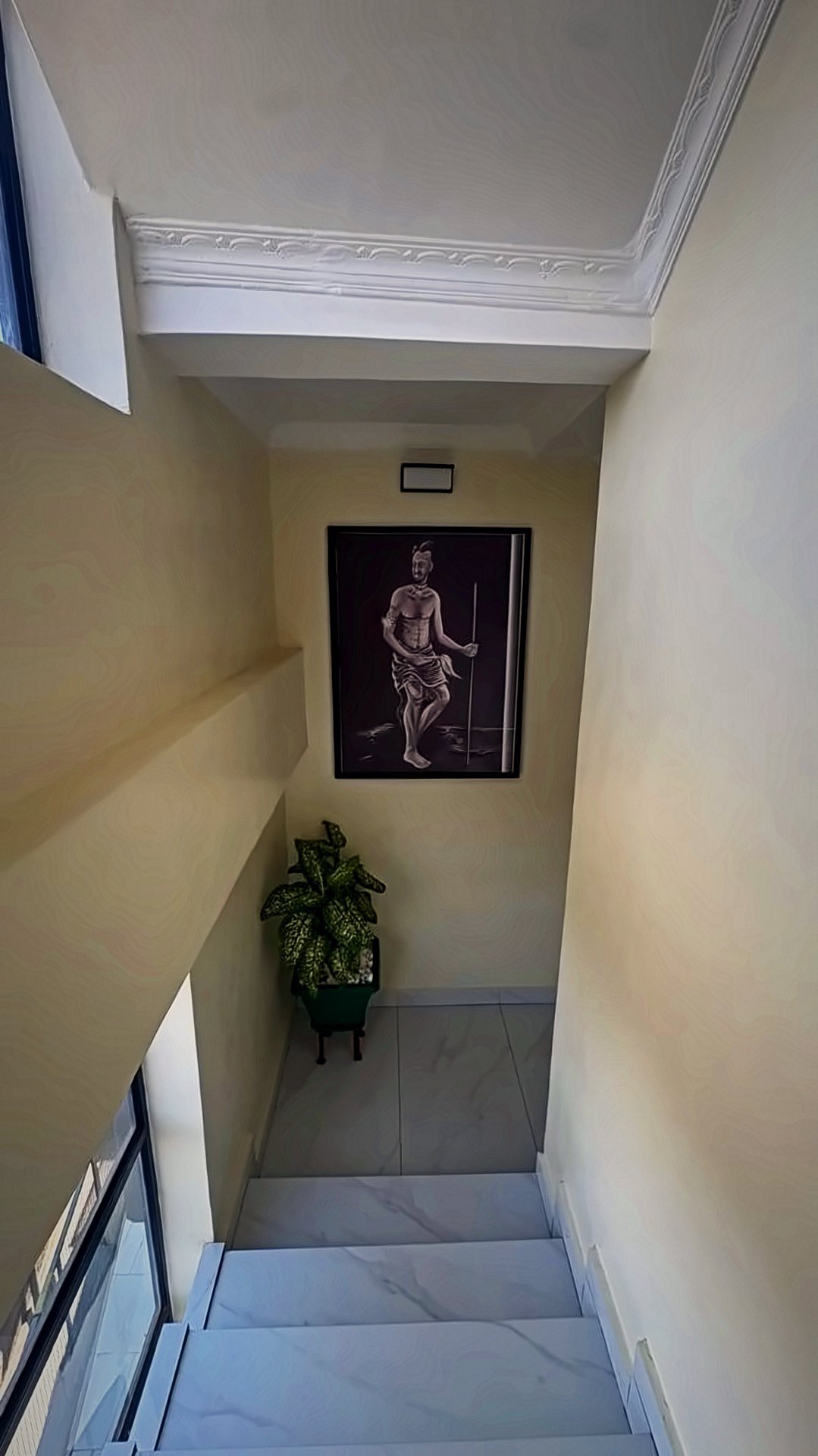 Staircase landing with a framed artwork and a plant at Holy Apartments, Kigali