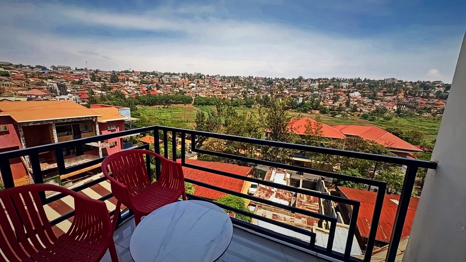 Balcony with two red chairs and a marble table above the rooftops of Kigali at Holy Apartments