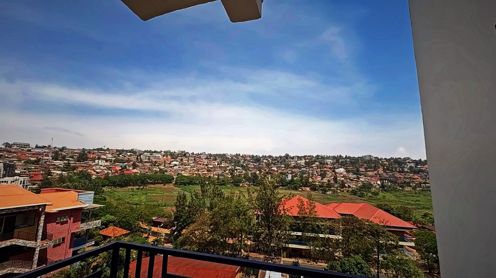 Wide view over Kigali neighbourhoods and green valley under a blue sky from a balcony at Holy Apartments