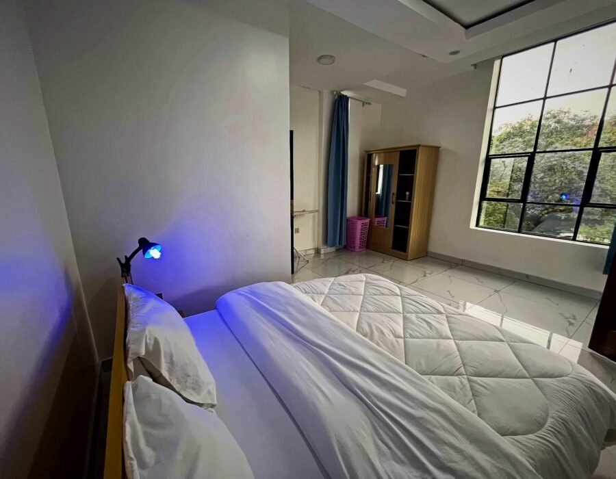 Bedroom with a large bed and a big window overlooking trees at Holy Apartments, Kigali